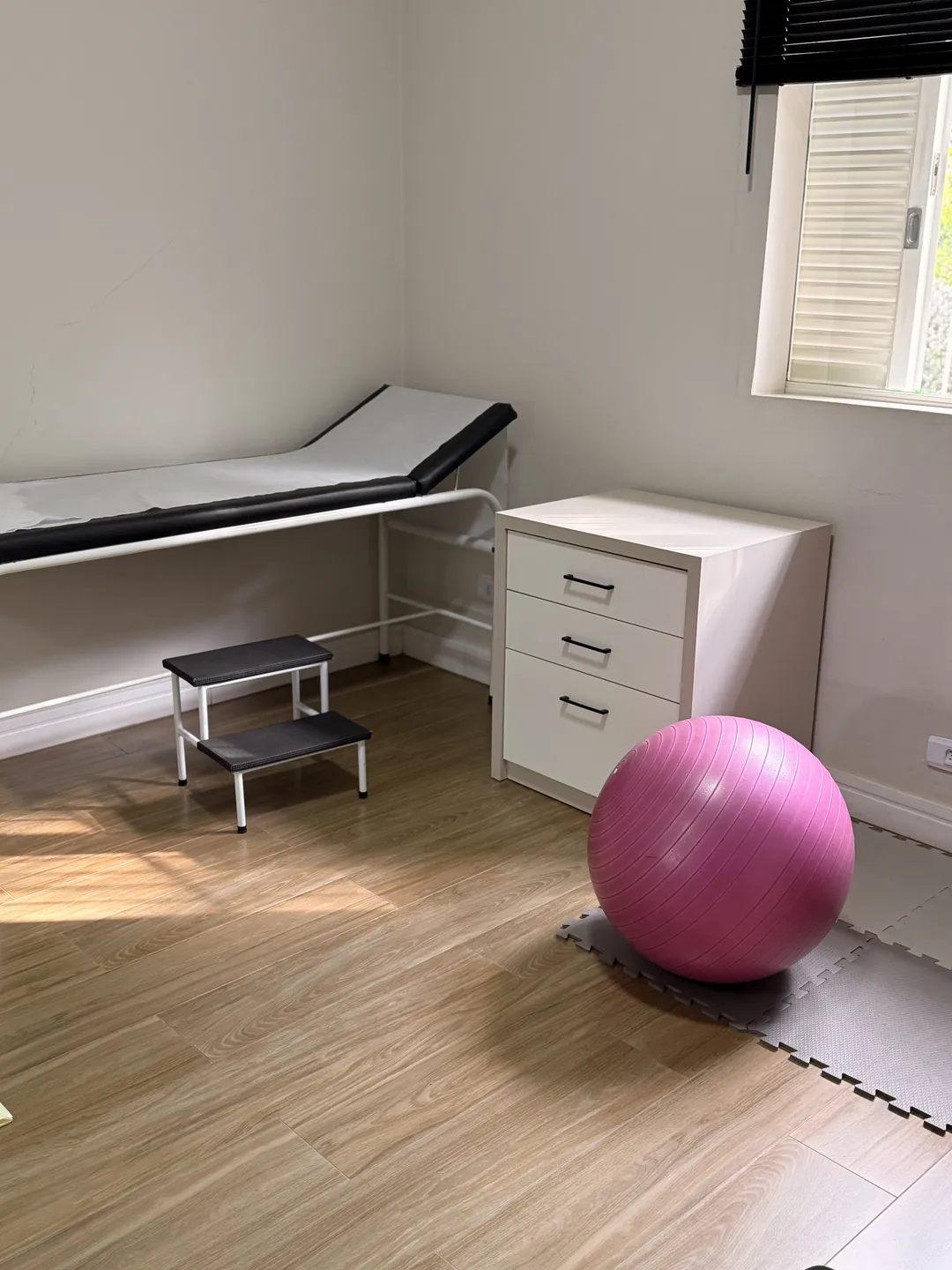 Sala de atendimento com maca, degrau e bola de exercício, na Clínica Luz.