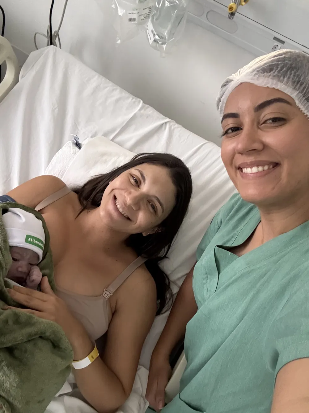 Mãe com o recém-nascido no quarto da maternidade, ao lado da Dra. Paula Bufarah de touca.