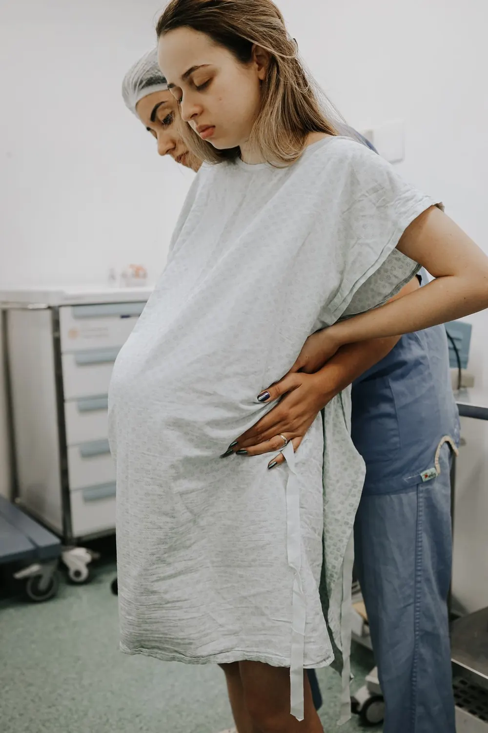 Doula apoia uma gestante em trabalho de parto, em pé, com as mãos na barriga.