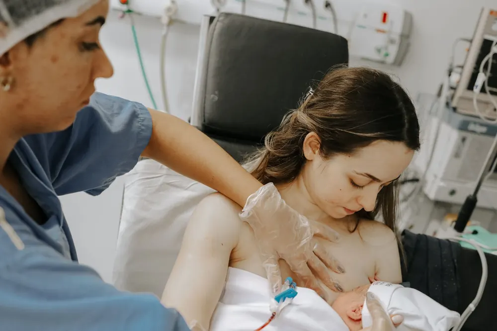Doula ao lado da mãe com o recém-nascido no colo, logo após o parto.