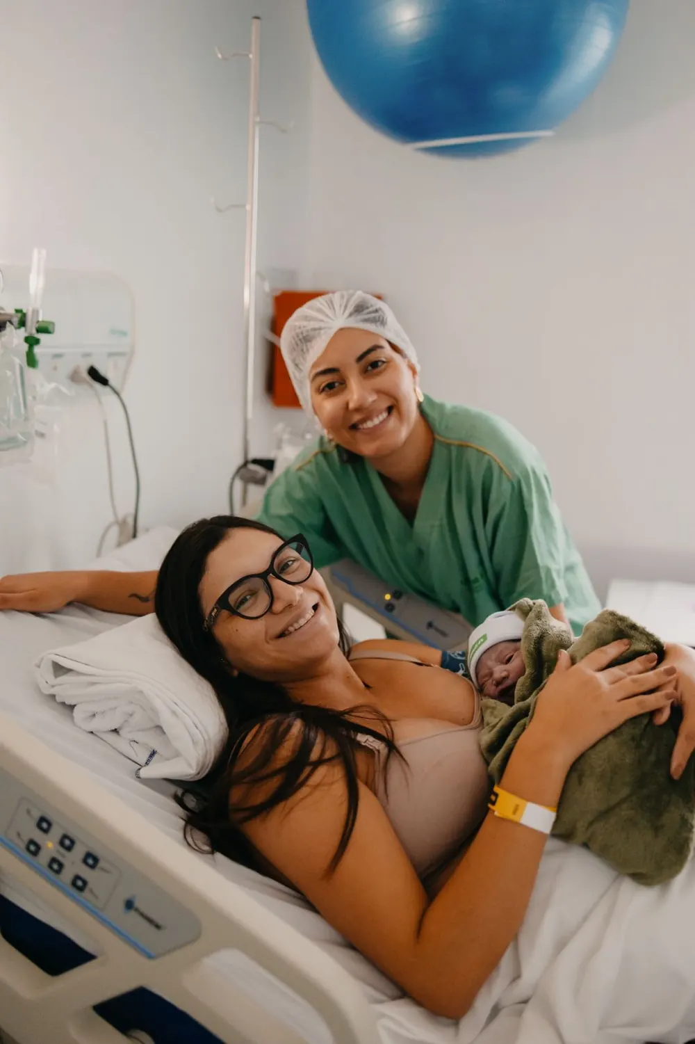 Mãe com o recém-nascido no colo na maternidade, com a Dra. Paula Bufarah ao lado.