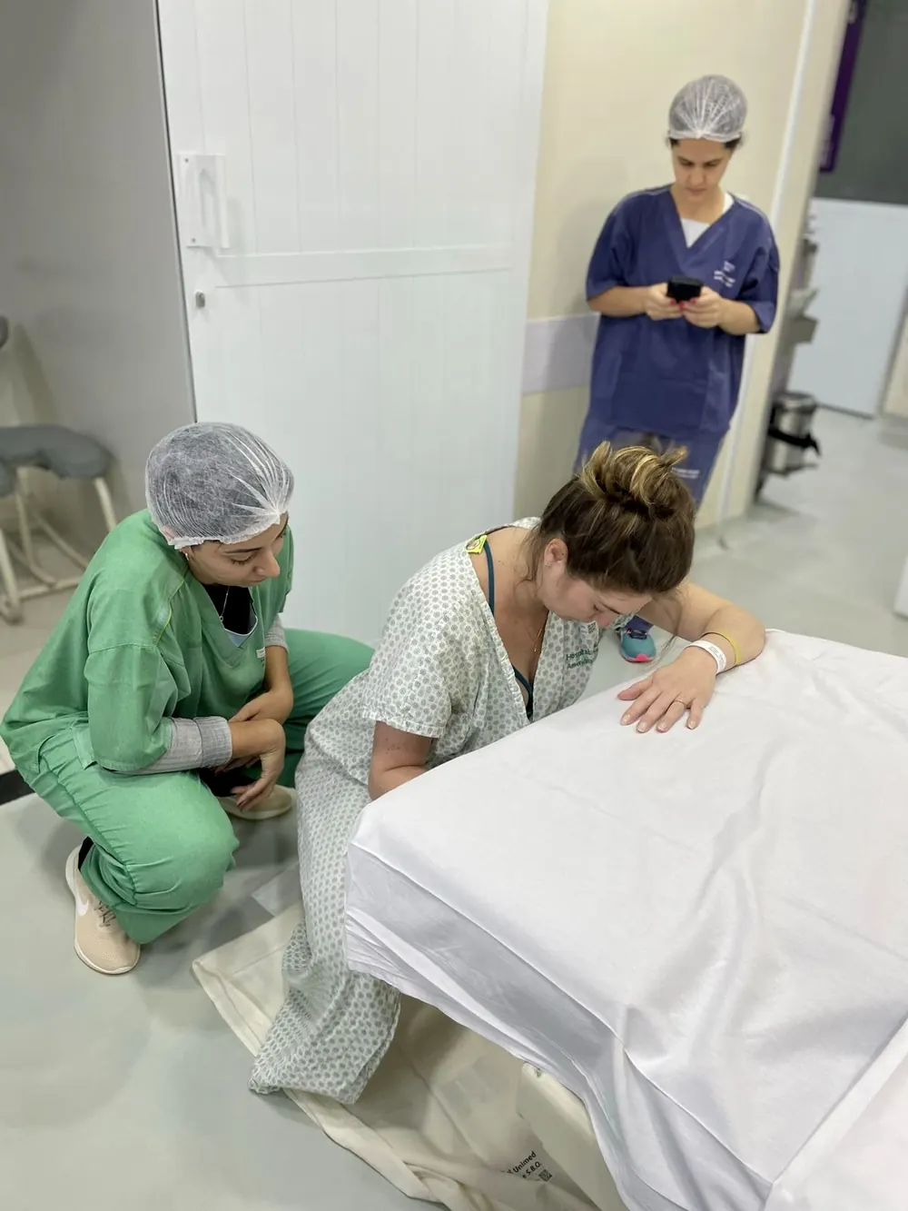 Doula agachada ao lado de uma mulher em trabalho de parto apoiada na cama.